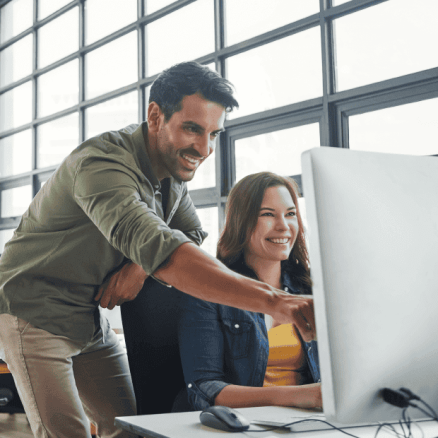 A compliance consultant in smart-casual clothing points to a laptop where a female professional is doing Payment Card Industry (PCI) data security training.