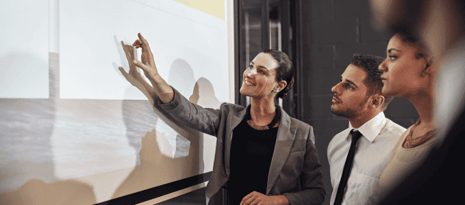 A professional woman points to a presentation as Xcina’s PCI DSS compliance services team discuss a client’s PCI audit results.