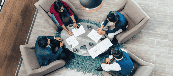 A team of certified auditors discuss PCI DSS gap analysis and compliance validation around a coffee table with papers on it. 